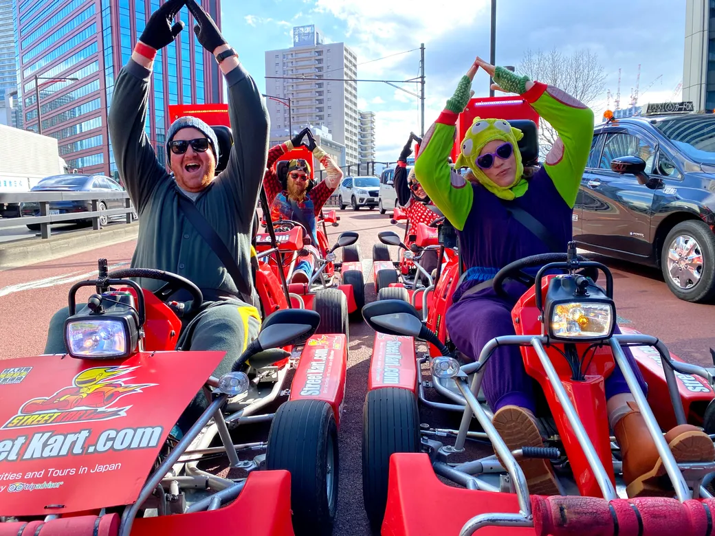 Group of people in red go-karts on a city street, arms raised in celebration.